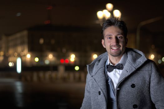 Attractive young man at night in Piazza Vittorio Veneto in Turin, Italy, wearing wool coat and bowtie