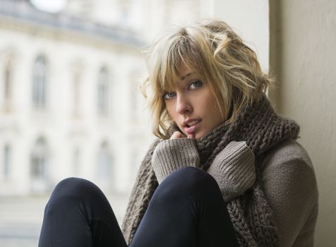 Attractive blonde young woman sitting next to window, elegant building in background