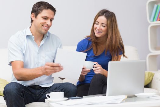 Smiling couple paying their bills online with laptop in living room at home