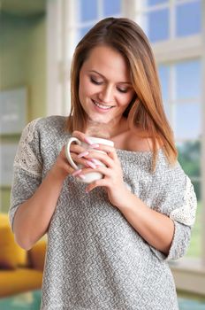 Woman smelling a cup of coffee, ready to drink it, in a room