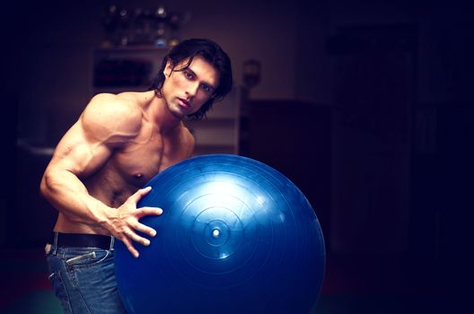 Muscular young man shirtless holding fitness or exercise ball