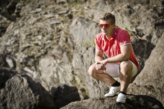 Handsome young man sitting on rock with sunglasses, looking to a side