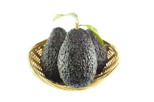 Avocados with leaves on a Dish of straw.