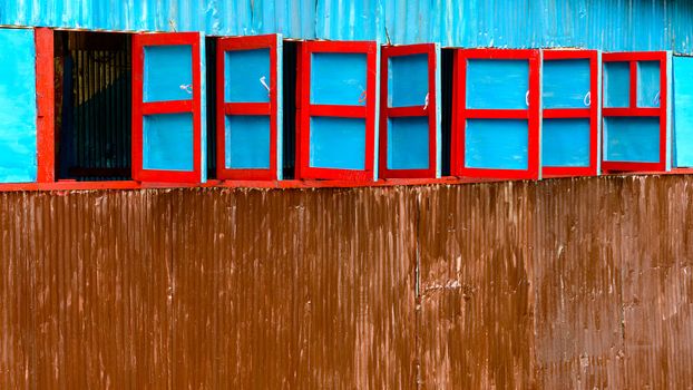 Red and blue wooden windows on corrugated steel wall, Nepal