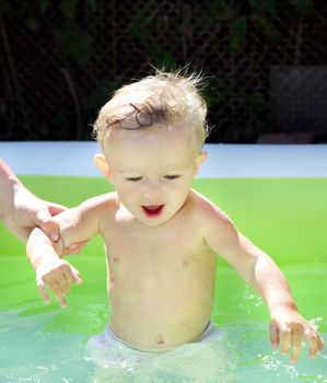 Parent bathing Cheerful Baby Boy in the Pool at Sunny Summer Day