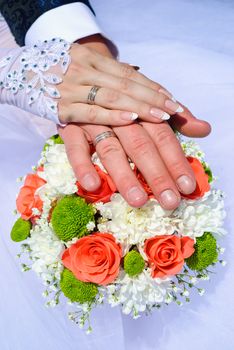 Hands of the groom and the bride with wedding rings on top of the bride's bouquet