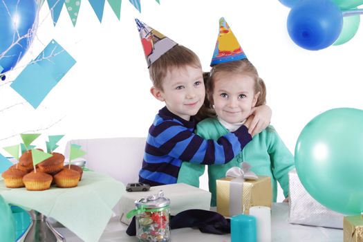 Two children huging at blue party table over white