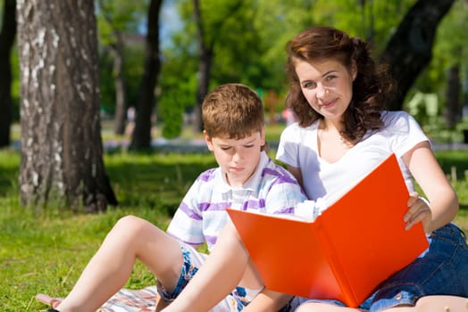 boy and a woman in a summer park reading a book together