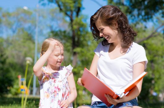 girl with the teacher reading a book together in the summer park