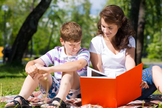 boy and a woman in a summer park reading a book together