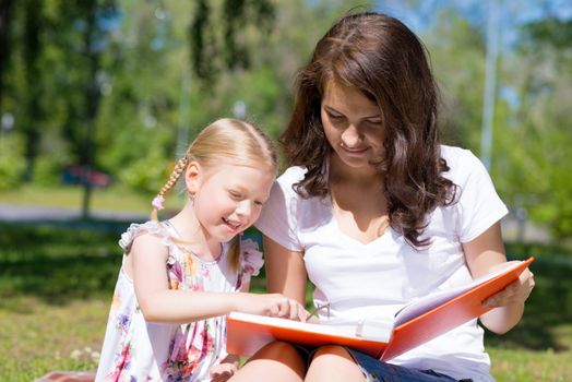 girl with the teacher reading a book together in the summer park