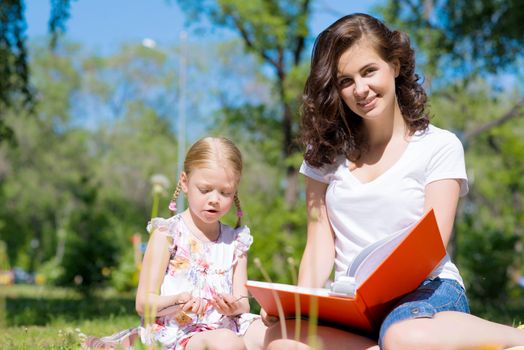 girl with the teacher reading a book together in the summer park