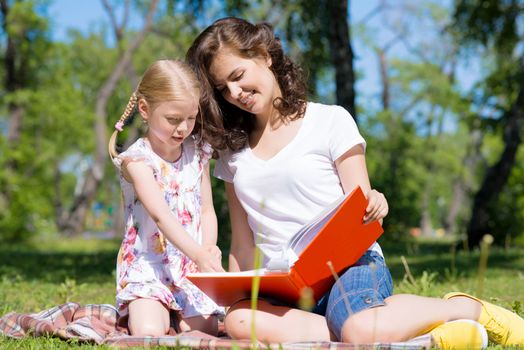 girl with the teacher reading a book together in the summer park