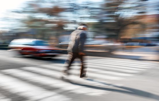 An elderly man crosses the street in a crosswalk. Intentional motion blur
