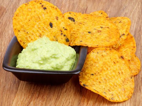 Arrangement of Tortilla Chips and Guacamole Sauce in Black Bowl closeup on Wooden background