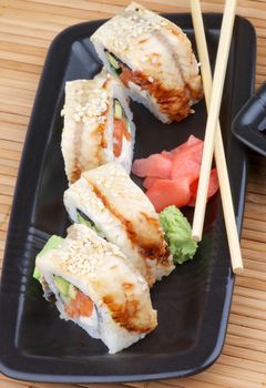 Arrangement of Unagi Sushi Rolls with Wasabi, Marinated Ginger with Pair of Chopsticks on Straw mat background