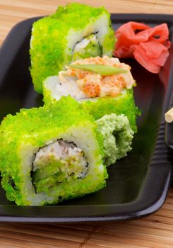 Delicious Maki Sushi with Avocado and Green Caviar Garnished with Marinated Ginger in Black Plate on Straw mat background