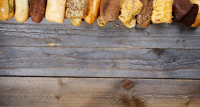 Frame of Various Buns, Baguette, Poppy Seed and Sesame Buns, Rye and Whole Wheat Bread closeup on Rustic Wood background