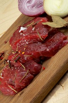 Arrangement of Raw Sliced Beef with Halves of White and Red Onion and Spices closeup on Wooden Cutting Board