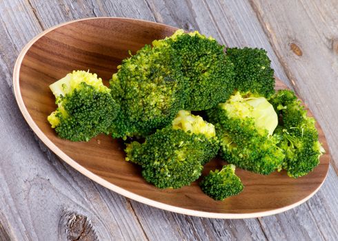 Tasty Ready-to-Eat Boiled Broccoli on Wooden Plate isolated on Rustic Wood background