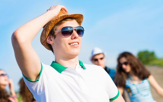 young man in sunglasses, a hat holds a hand on a background of blue sky and friends