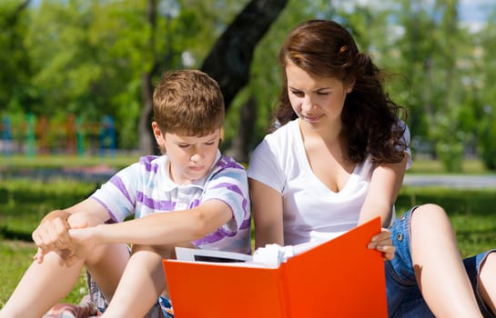 boy and a woman in a summer park reading a book together