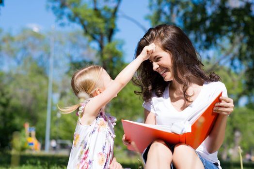 girl with the teacher reading a book together in the summer park