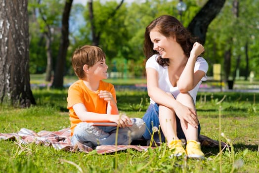 boy and a woman in a summer park reading a book together