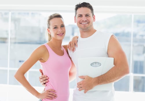 Portrait of a fit couple holding weighing scale in bright exercise room