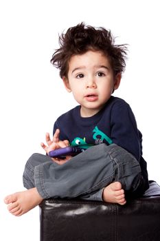 Cute toddler boy sitting with mobile device and crazy hair, isolated.