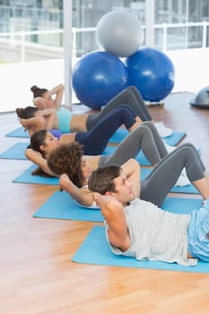 Side view of determined young people doing sit ups in the fitness studio