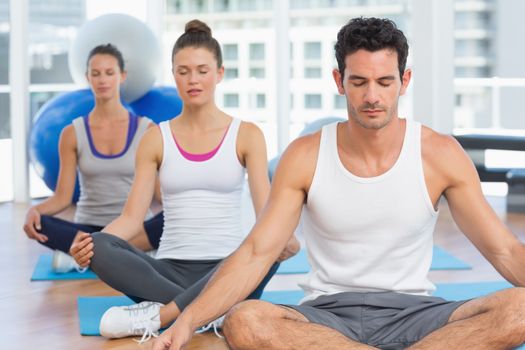 Three sporty young people in meditation pose with eyes closed at a bright fitness studio