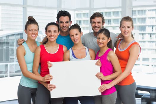 Portrait of fit smiling young people holding blank board in a bright exercise room