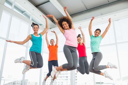 Full length portrait of fitness class and instructor jumping in fitness studio