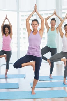 Portrait of a fit class standing in tree pose at a bright fitness studio