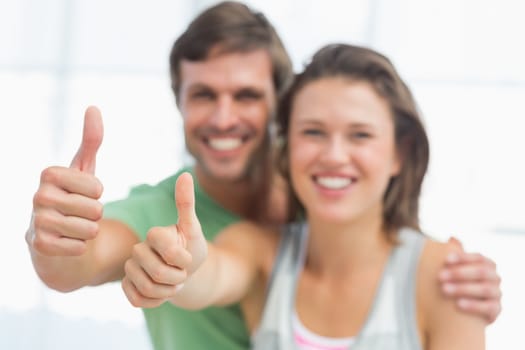 Portrait of a fit young couple gesturing thumbs up in bright exercise room