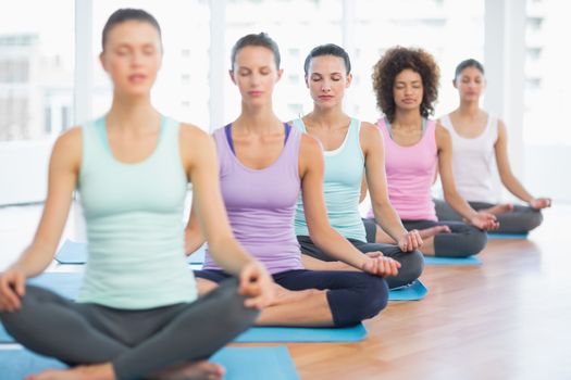 Sporty young women in meditation pose with eyes closed at a bright fitness studio