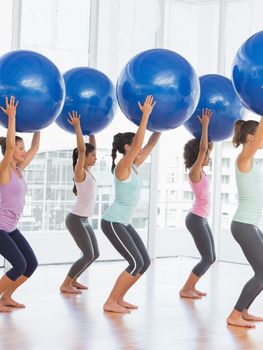 Full length side view of fit young women holding blue fitness balls in exercise room