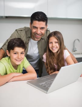 Portrait of a smiling father with young kids using laptop in the kitchen at home