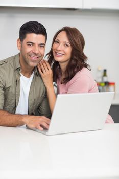 Portrait of a happy couple using laptop in the kitchen at home