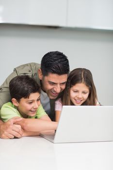 Father with young kids using laptop in the kitchen at home