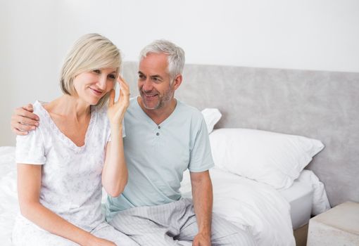 Smiling mature man and woman sitting on bed at home