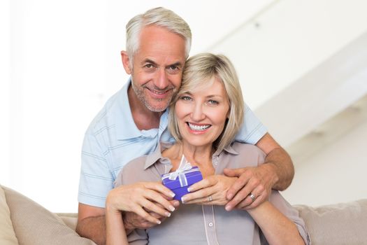 Portrait of a smiling mature man surprising woman with a gift on sofa at home