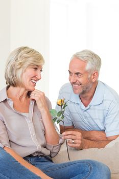 Mature man giving a flower to a smiling woman sitting on couch at home