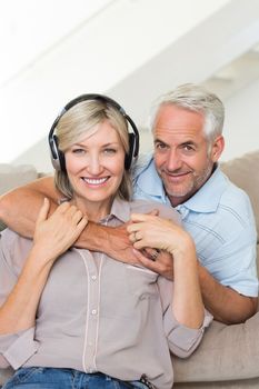Smiling mature man embracing woman from behind on sofa at home