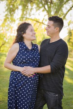 Happy Hispanic Man With His Pregnant Wife Outdoors At The Park.