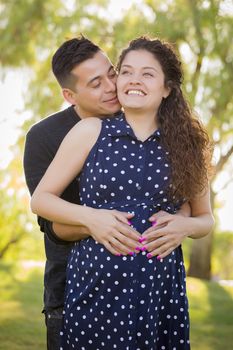 Happy Hispanic Man Hugs His Pregnant Wife Outdoors At The Park.