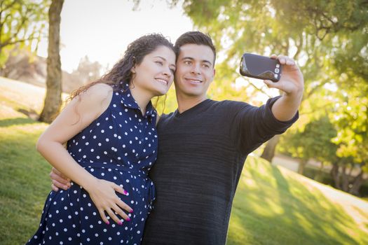 Pregnant Wife and Husband Taking Cell Phone Picture of Themselves Outdoors At The Park.