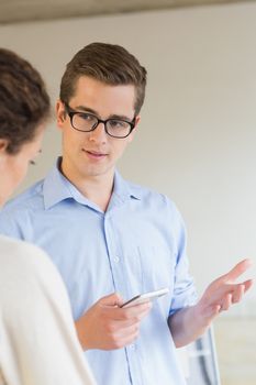 Young businessman holding mobile phone while communicating with female colleague in office