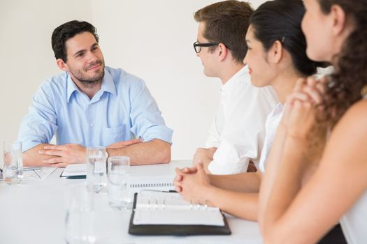 Confident young businessman discussing with colleagues in meeting at office